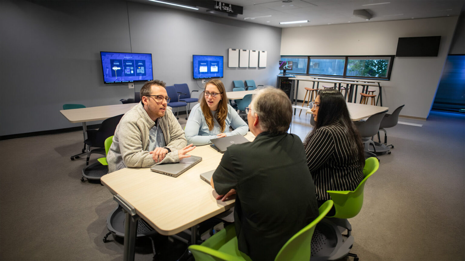 A group of people talking with their laptops on the desk in a classroom background