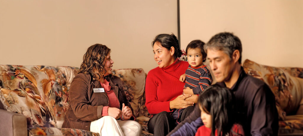 A Nipissing student talking to a mom in red holding her baby with the dad in front with their other child