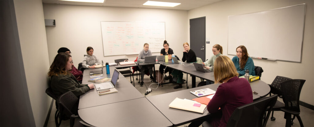 A group of students and professor sitting around for a discussion in a classroom setting