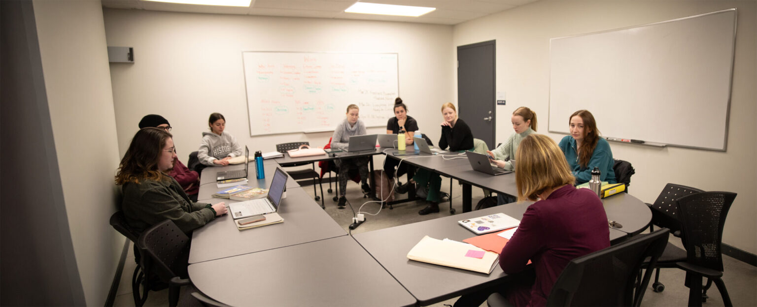 A group of students and professor sitting around for a discussion in a classroom setting