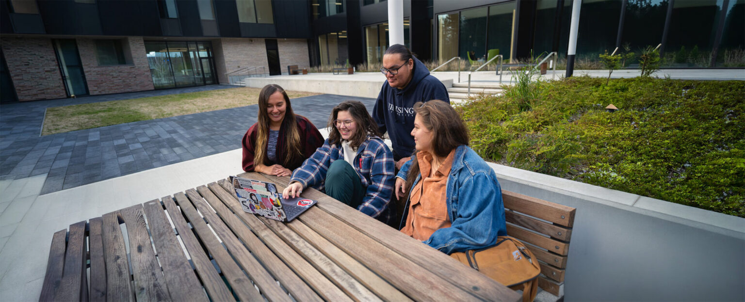 4 students sitting on a bench outside the student centre