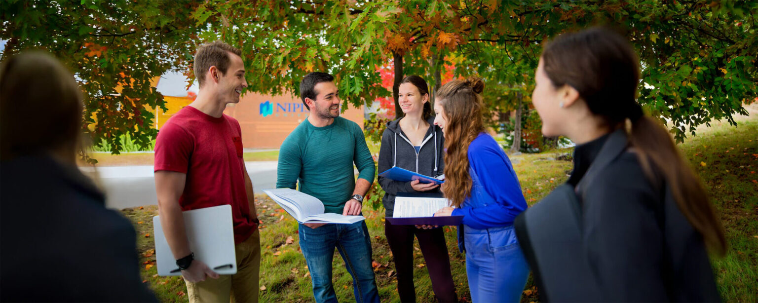 5 students talking with books outside in the fall scene near the Nipissing entrance