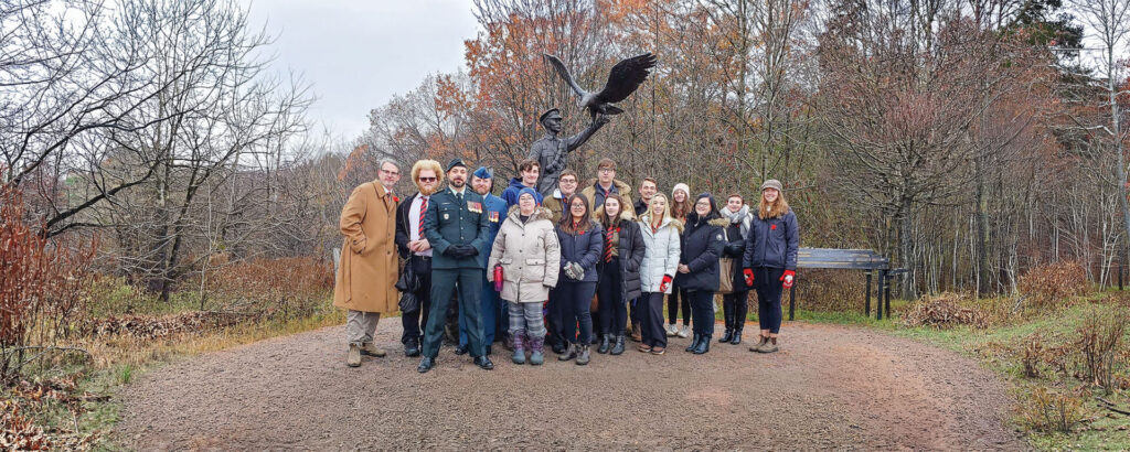 A picture of a group field trip with a historical statue behind them in a nature setting