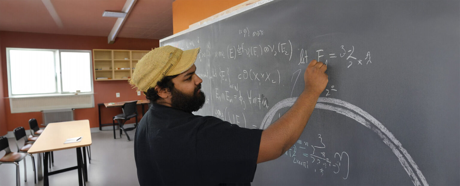 A student in black top writing equation with chalk on the black board
