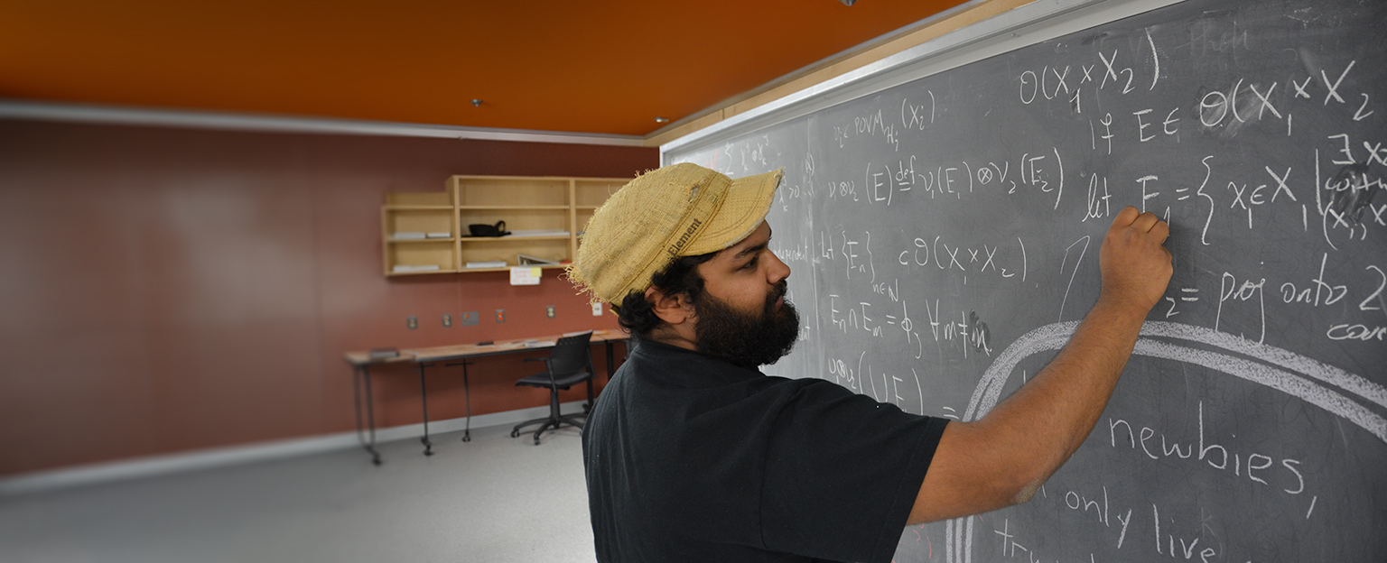 A student in black top writing equation with chalk on the black board