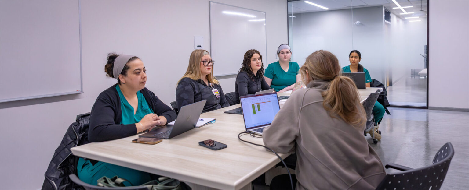 A group of nurses in scrubs working on their laptop in the nursing lab