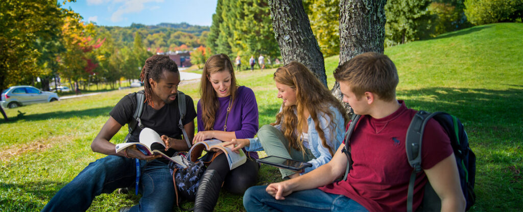 4 students sitting on the grass with Nipissing's entrance in the background