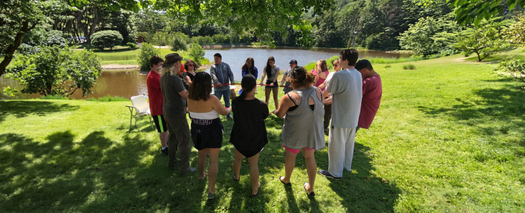 A group of students standing in a circle holding a rope outside