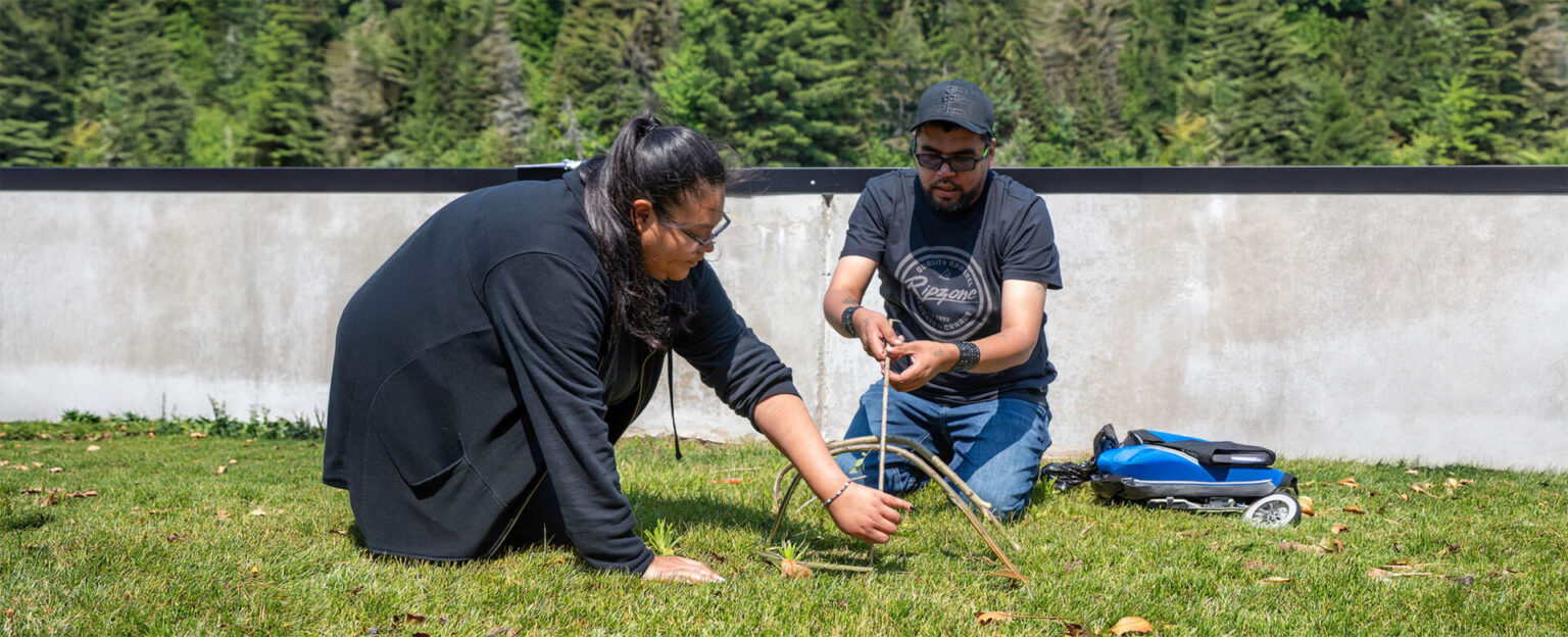 2 students building something out of tree branches outside on the grass
