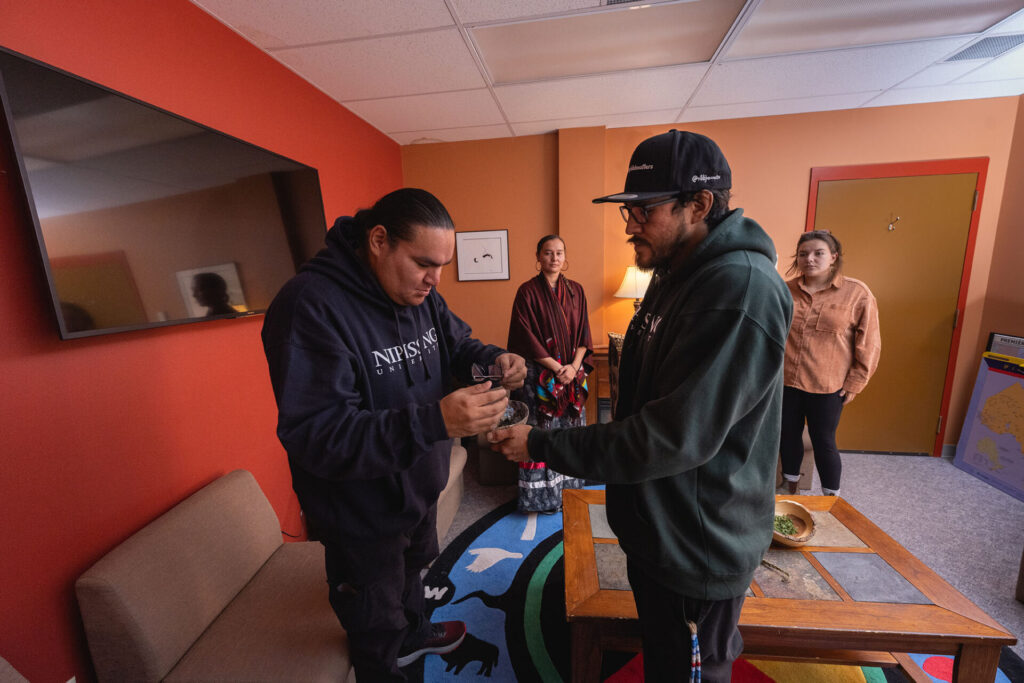 2 male students in green and blue hoodies performing an indigenous act in the sacred space
