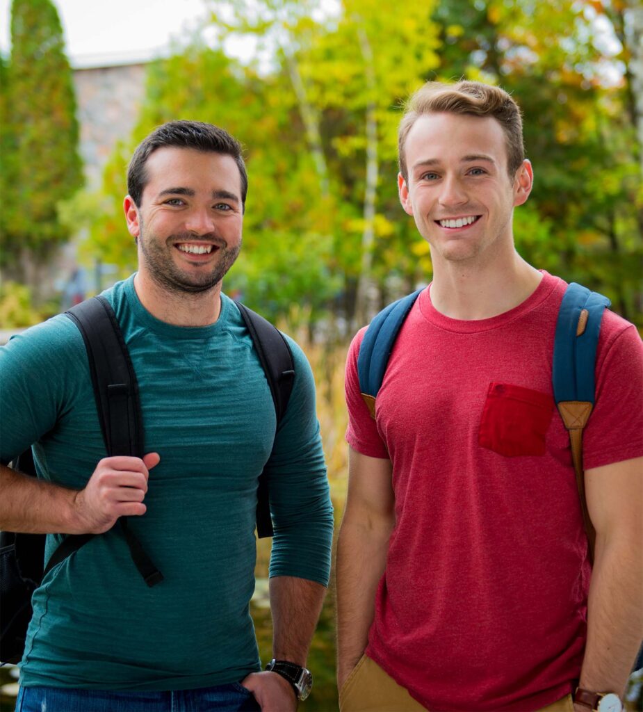 2 male students in green and red shirts standing outside with a nature background behind them