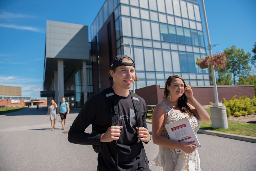 A male and female student walking outside with the library in the background behind them