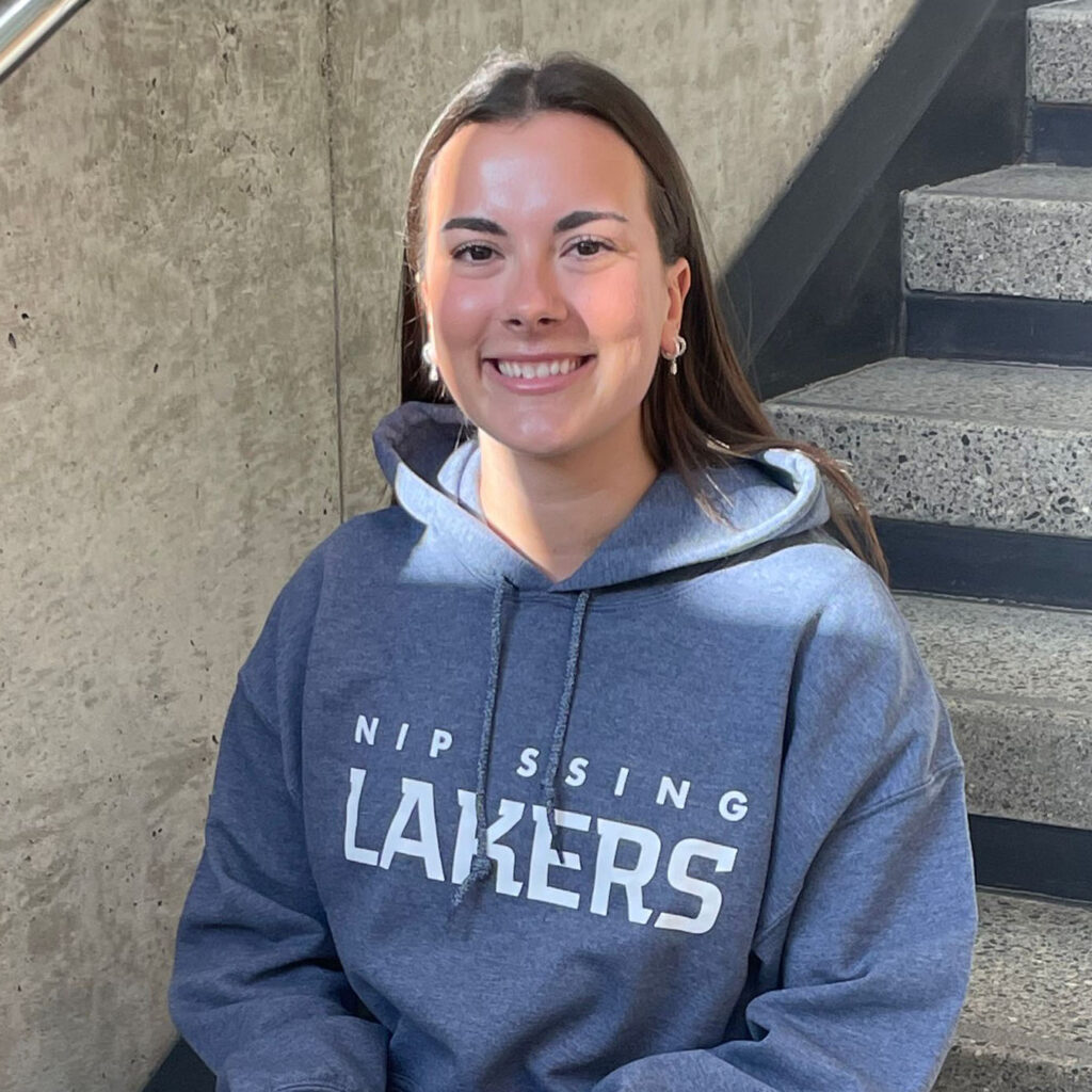A female student in grey laker hoodie sitting on the staircase