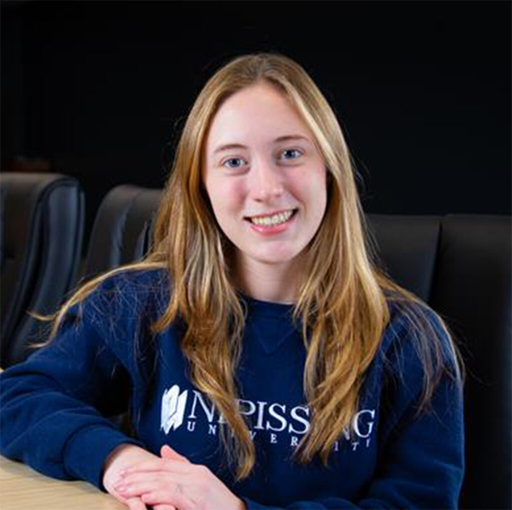 A female student in navy Nipissing sweater in front of a black background