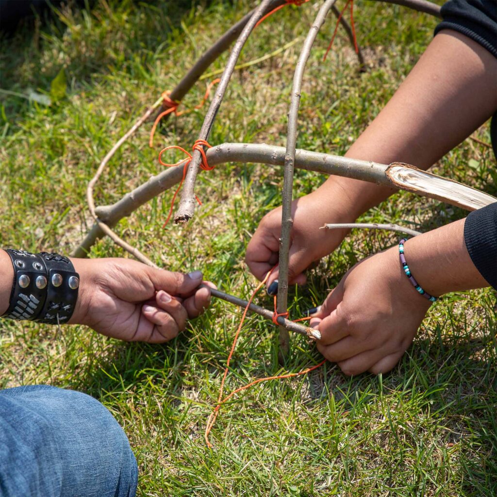 2 people's hands building something out of thin twigs