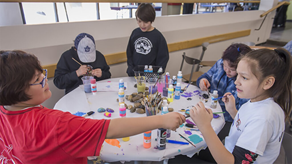 A group of Indigenous children painting on the table in the cafeteria