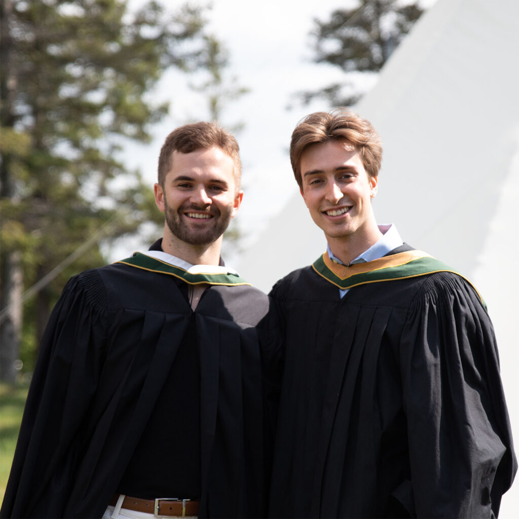 2 graduate in convocation gowns posing outside