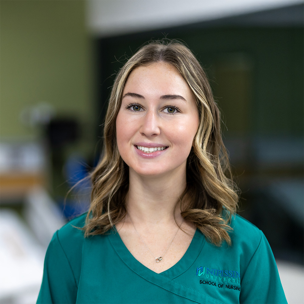 A student in green nursing scrub in front of a lab background