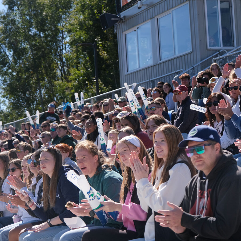A crowd of people cheering on benches watching a game