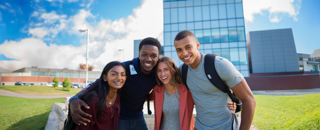 4 students with hands over shoulders with the library building in the background