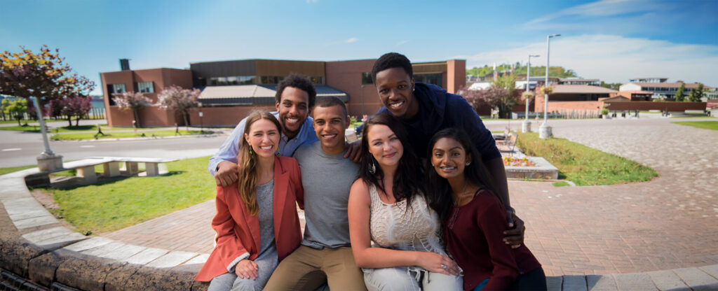 A diverse group of students gathered around with the Nipissing entrance behind them