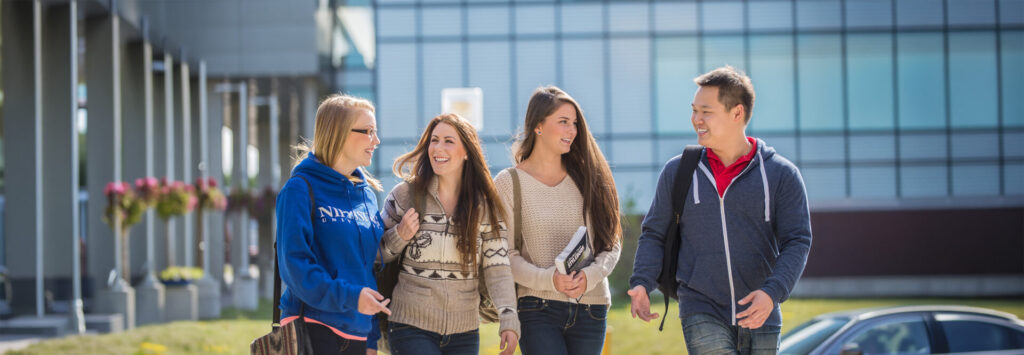 4 students talking and walking outside with the library building behind them