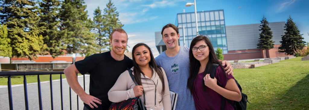 4 students standing next to each other with the library building within view in the background