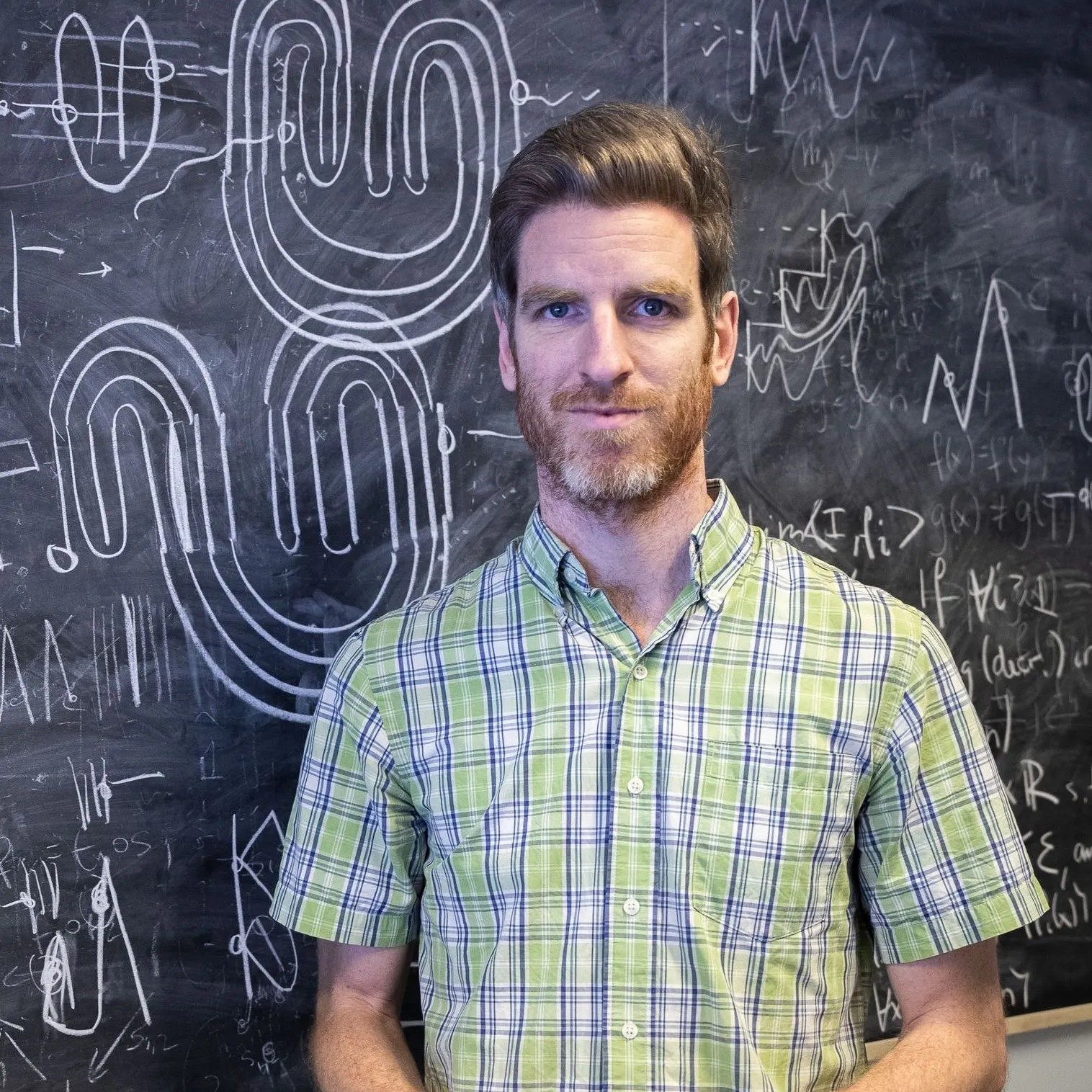 A professor in green checkered shirt in front of a black board