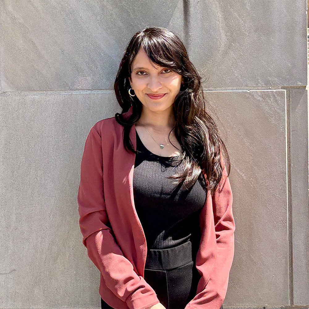A woman in black and pink top standing outside against a beige wall