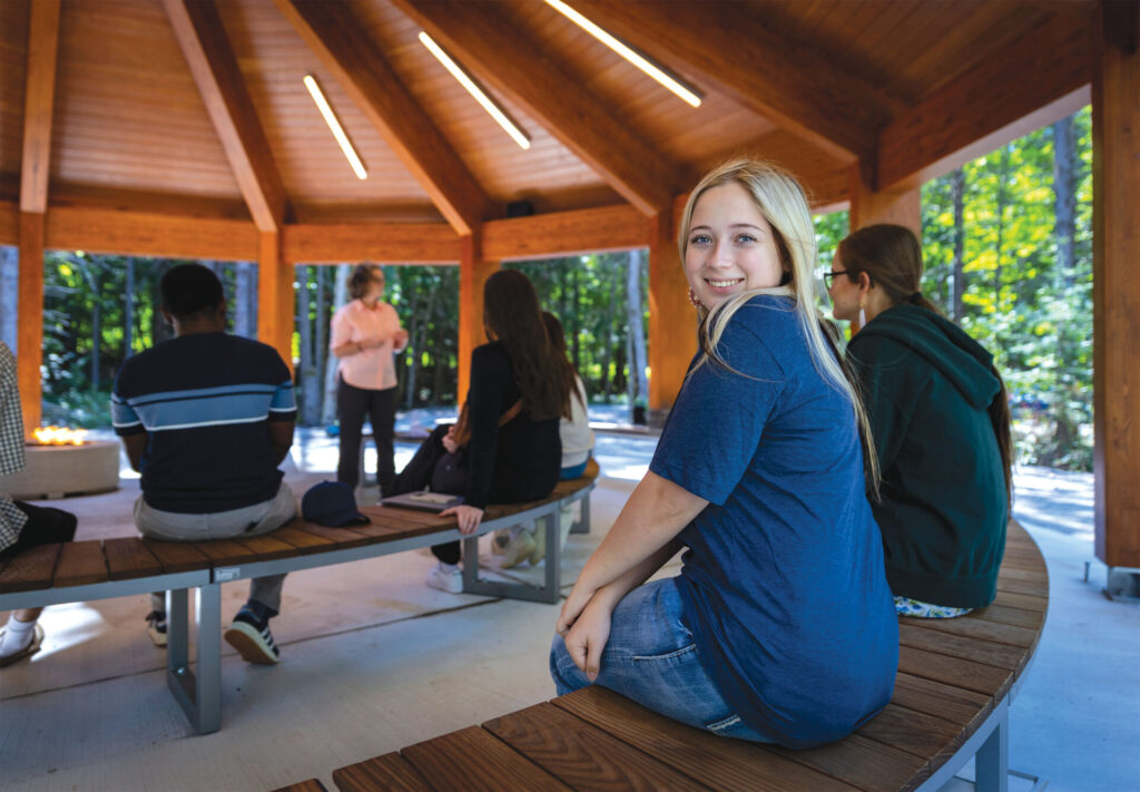 A female student facing the camera with a class going on at the outside classroom